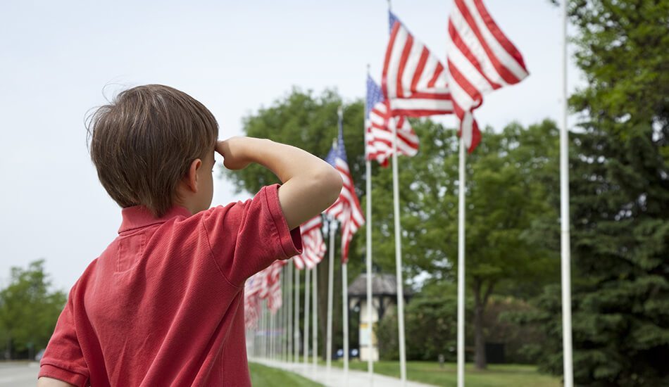 Young child saluting American Flags on Memorial Day | Ductless air conditioning | Stiles Heating, Cooling, & Plumbing